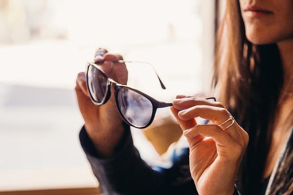 Trendy young female millennial adjusting sunglasses near fence in