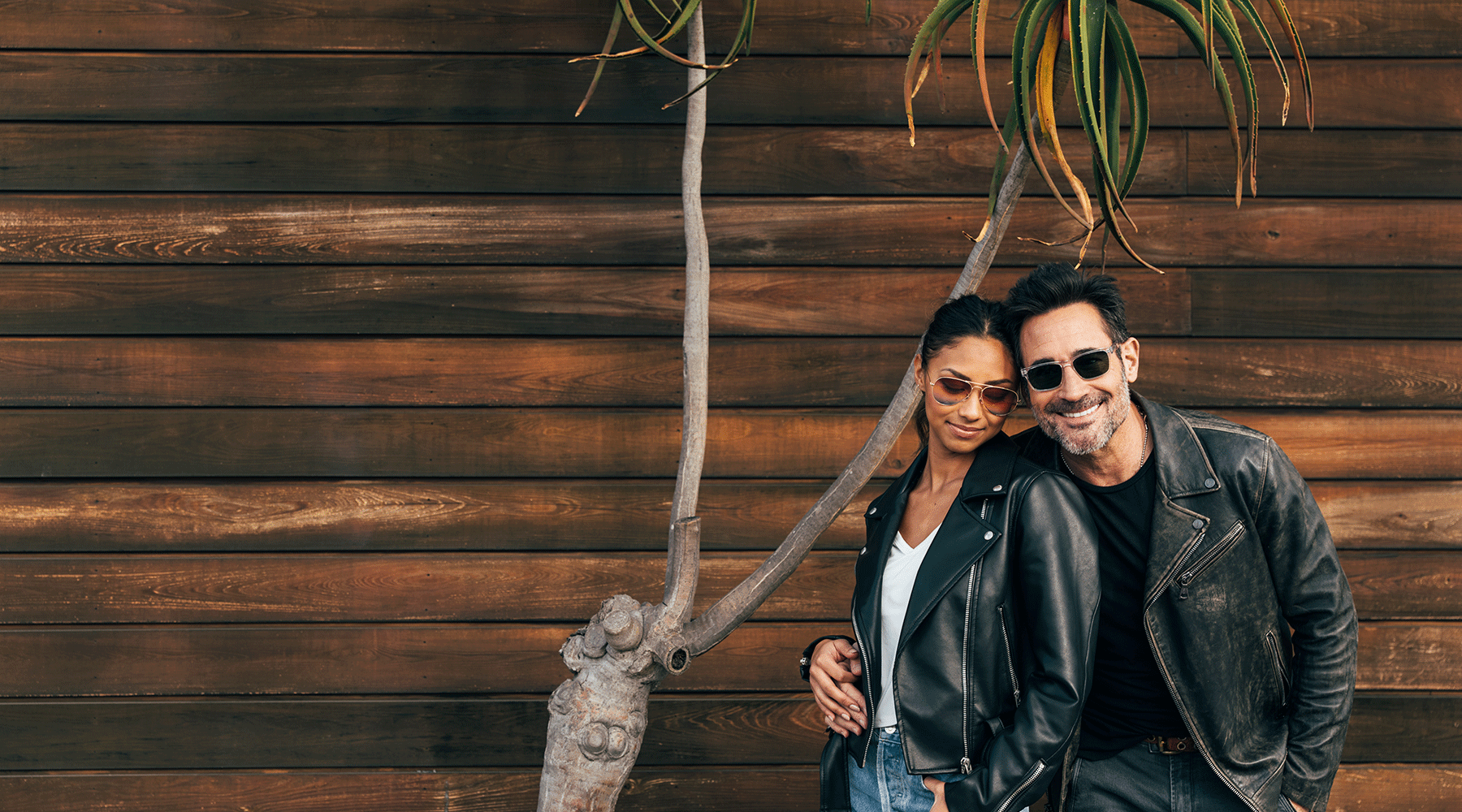 Man & Woman in Alexander Daas sunglasses against a wood wall next to a tree